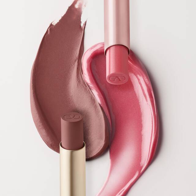 Un'immagine divisa che mostra prodotti cosmetici. A sinistra, sono visibili due campioni di prodotti per labbra rosa, uno in un rosa-marrone piu chiaro e l'altro in un rosa piu brillante e lucido. Un tubo di balsamo labbra Valentino Spike e un tubo di lucidalabbra sono posizionati accanto. Il lato destro mostra una confezione di Spike Valentino Disco Balm e una confezione di Spike Valentino Matte, con i rispettivi campioni di colore disposti sotto di essi.