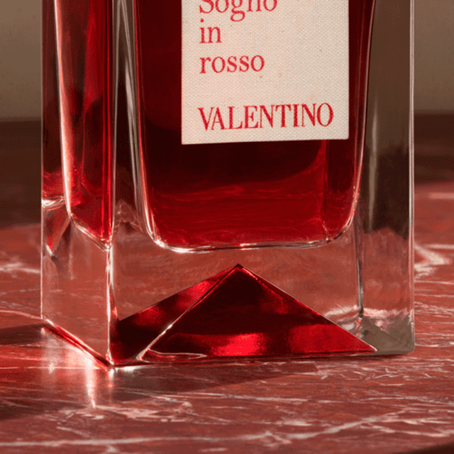 Un flacone di profumo di Valentino, con etichetta che recita "Sogno in rosso", posto su un tavolo di marmo rosso.