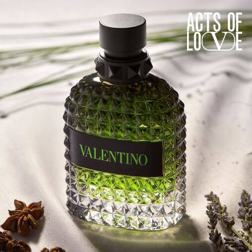 Flacone di profumo Valentino, con design elegante e tonalita verde, posizionato su un tessuto chiaro e decorato con erbe.
