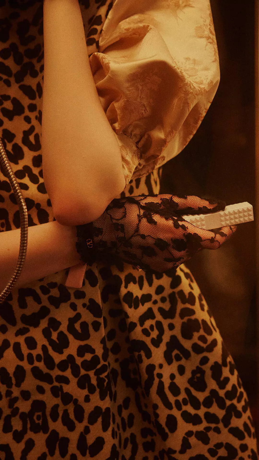 Una donna con guanti di pizzo neri, che tiene SPIKE VALENTINO IVORY, preme la tastiera di un telefono vintage.