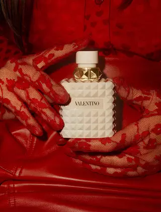 Una donna in rosso, che indossa guanti di pizzo rosso squisitamente decorati, tiene in mano BORN IN ROMA IVORY DONNA.