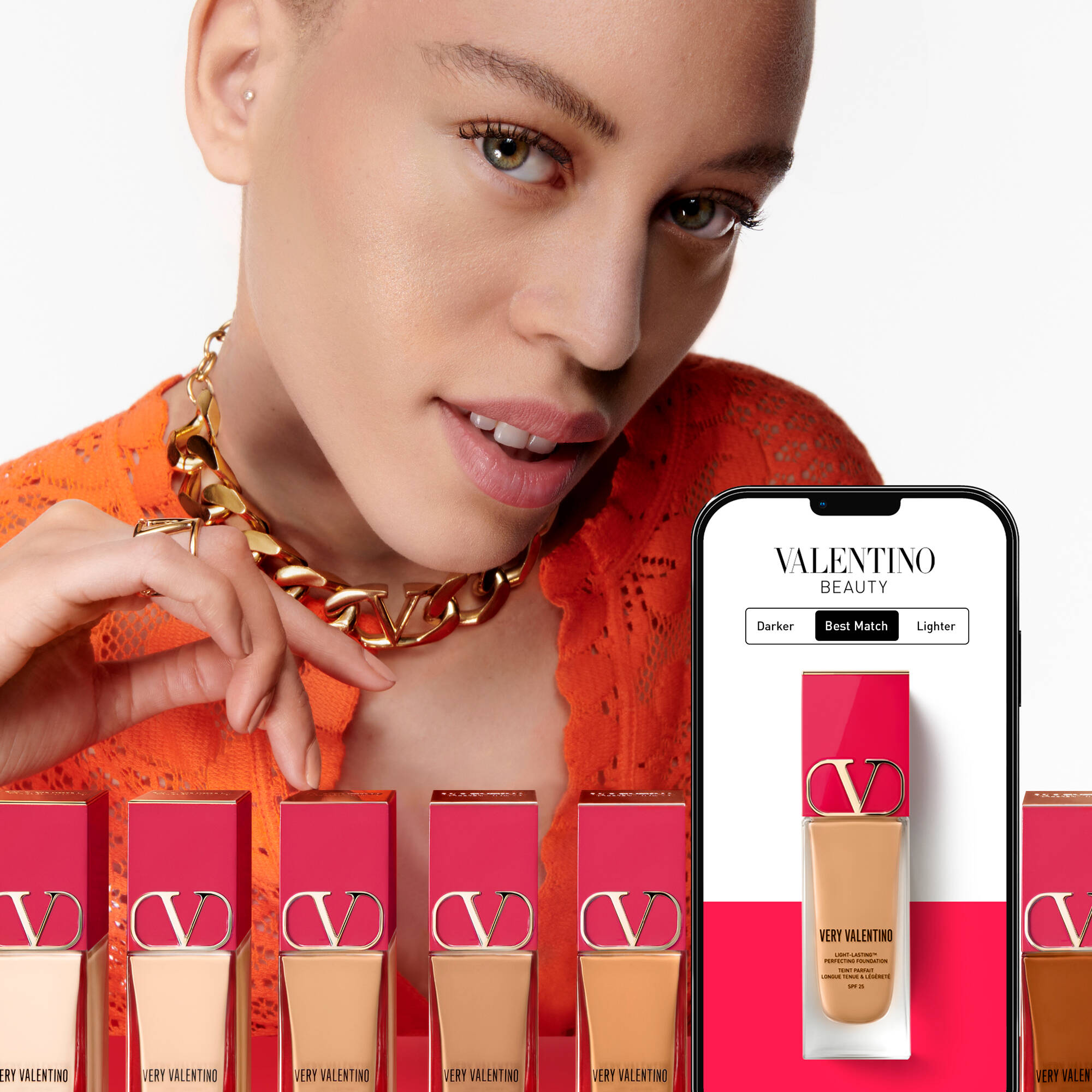 Modella con tratti distintivi, indossa un top arancione e collana dorata, posando vicino a una selezione di fondotinta e a un cellulare che mostra il sito di Valentino Beauty.