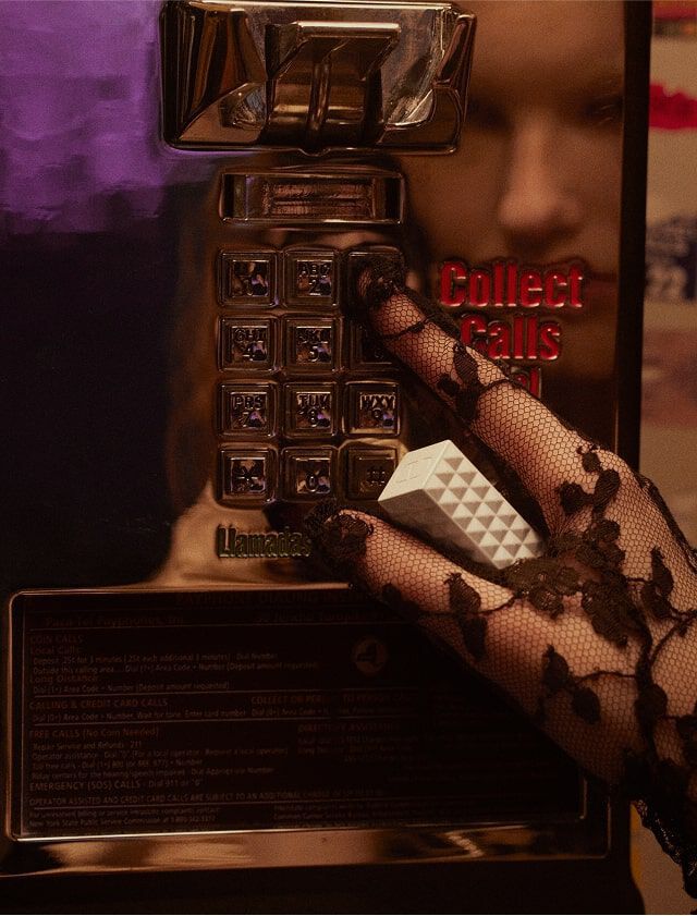 Una donna con guanti di pizzo neri, che tiene SPIKE VALENTINO IVORY, preme la tastiera di un telefono vintage.
